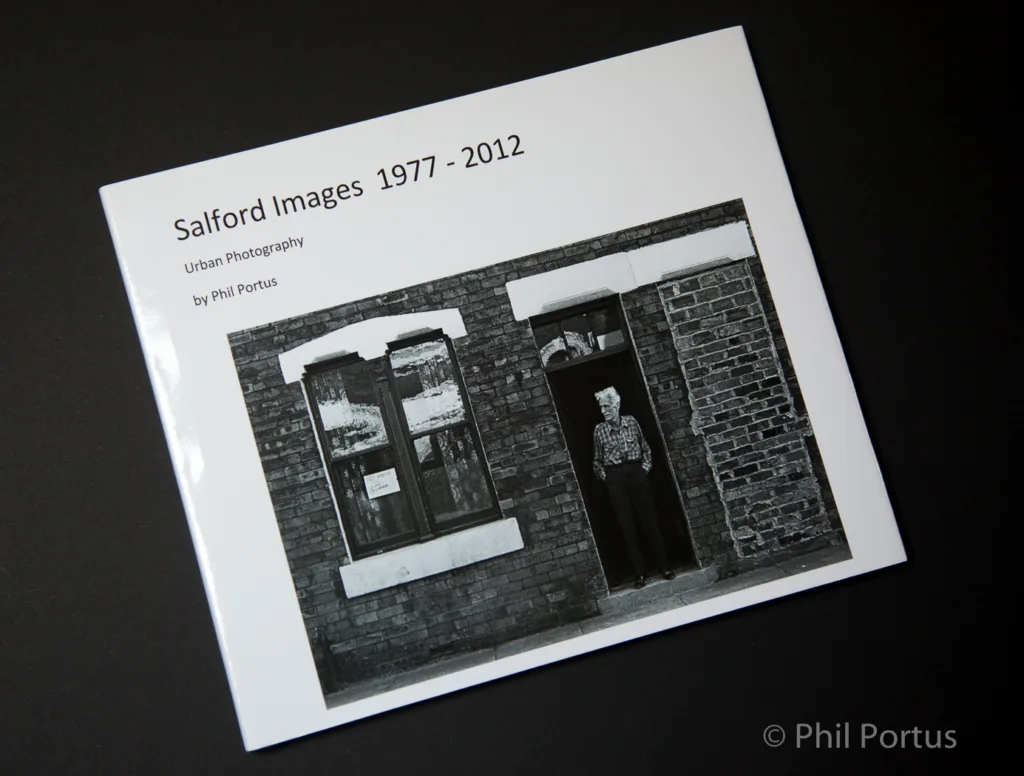 A black and white book lies angled on a dark surface with text and an image visible on its cover.
