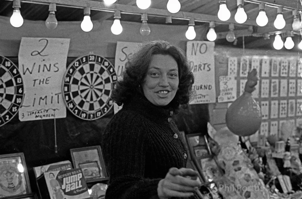A woman with curly hair smiles while standing in a room filled with games and string lights.