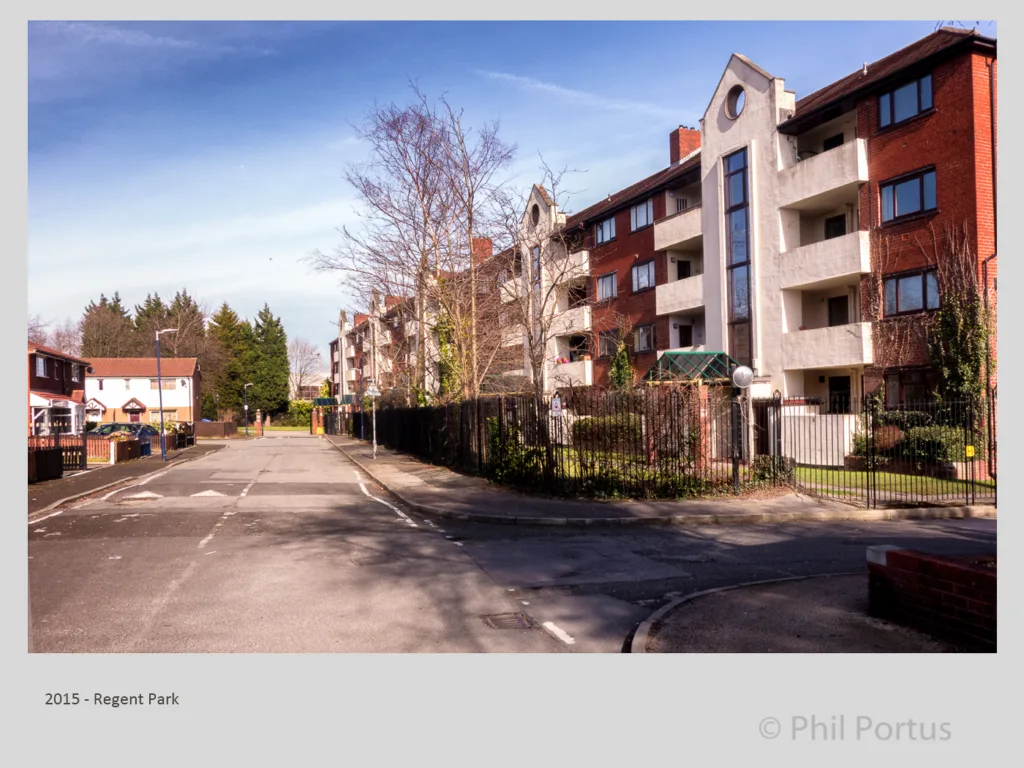 A residential street with brick apartment buildings and a detached house is visible under a bright sky.