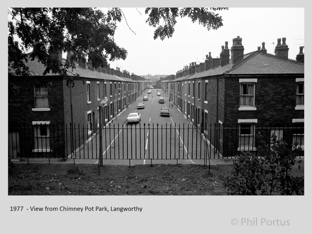 A black and white view looks down a street lined with brick houses and a wrought iron fence in the foreground.