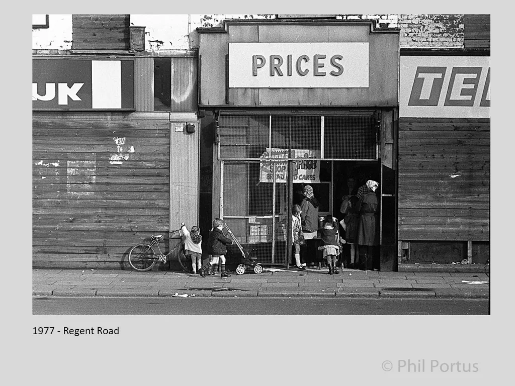 Black and white image shows a storefront with children gathered outside.