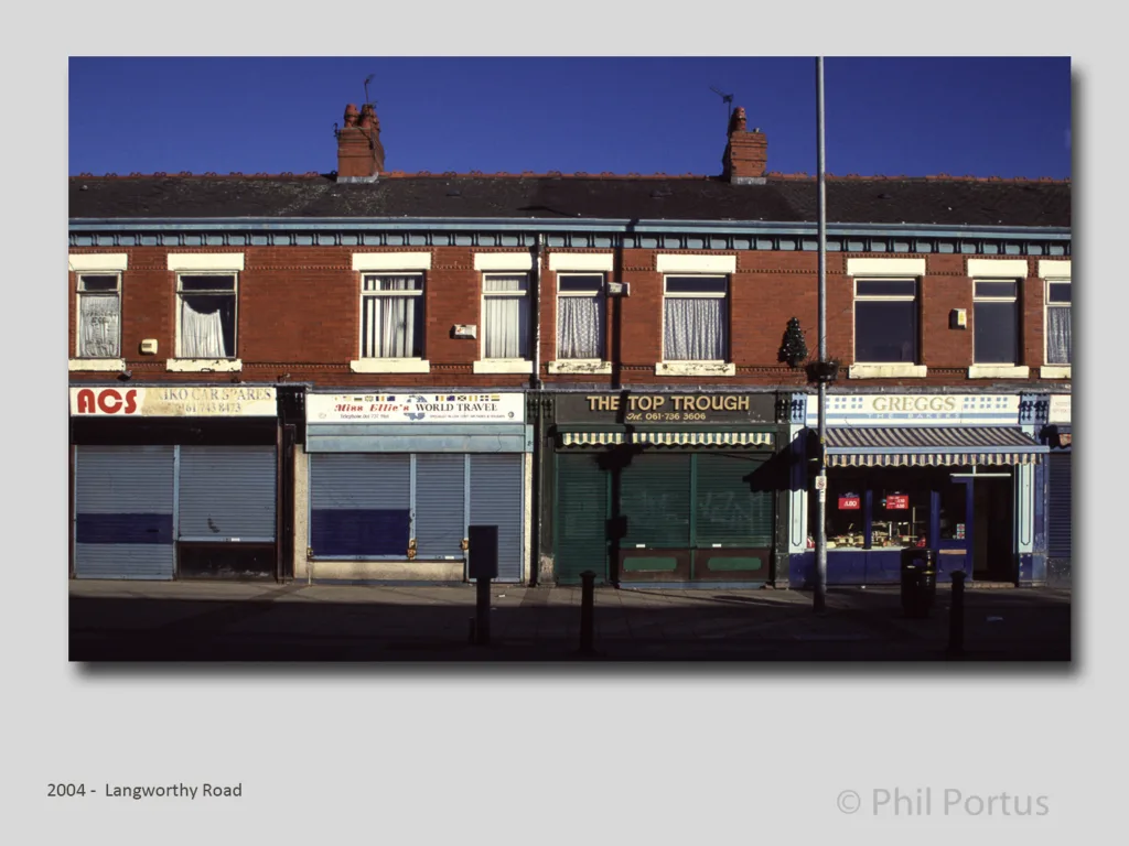 A row of brick storefronts with closed shutters sits beneath a clear blue sky.