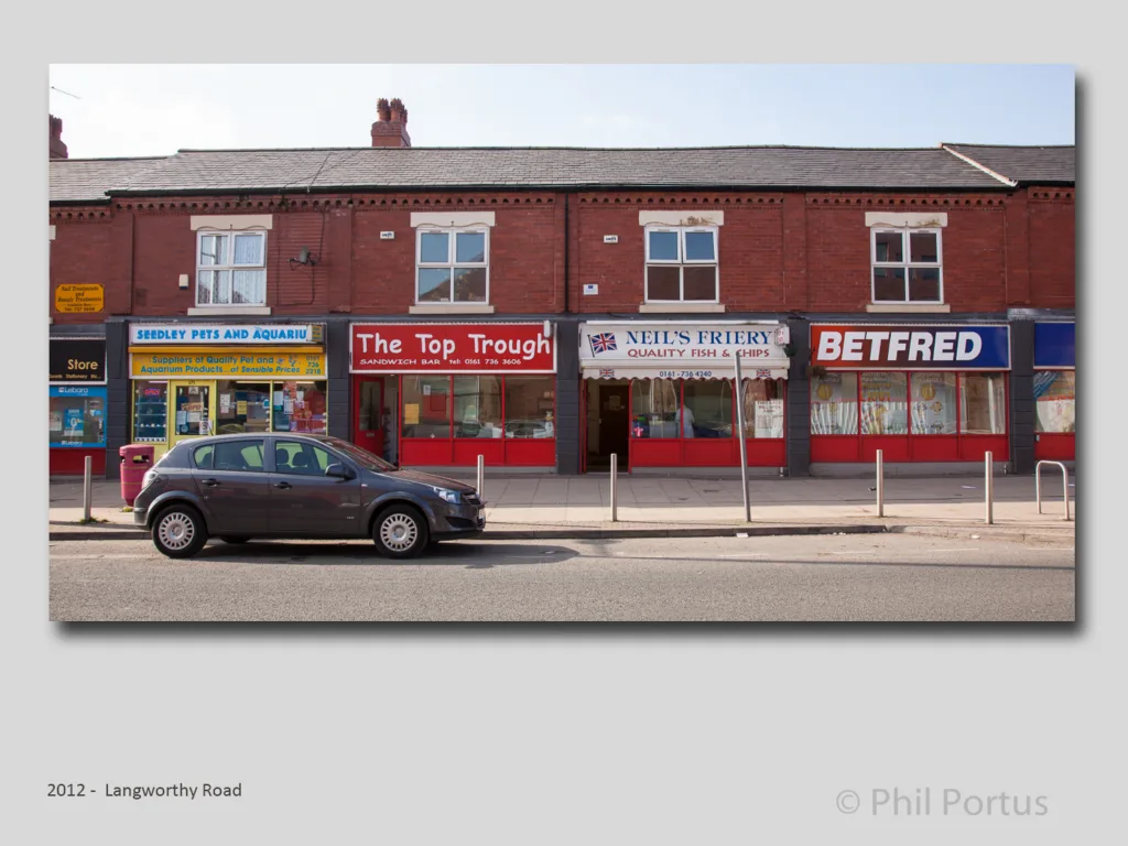 A row of brick storefronts with signs and a dark car parked in front of them.