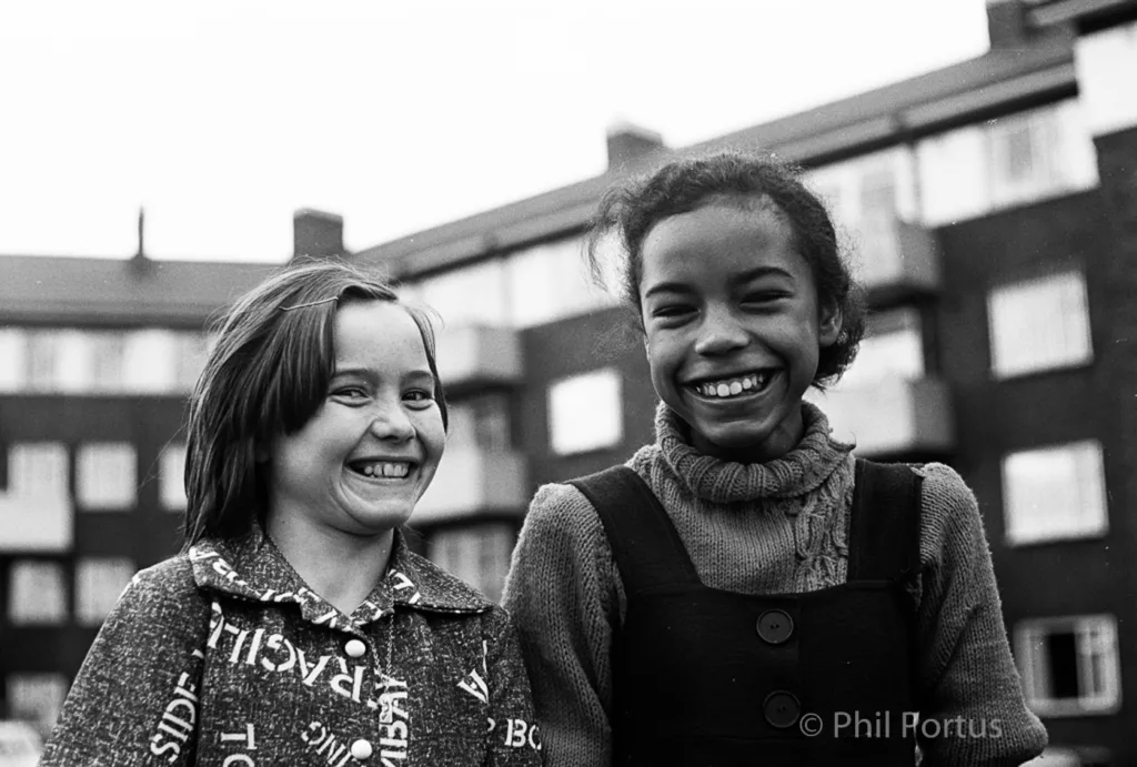 Two smiling children wearing sweaters look directly at the camera in a black and white portrait.