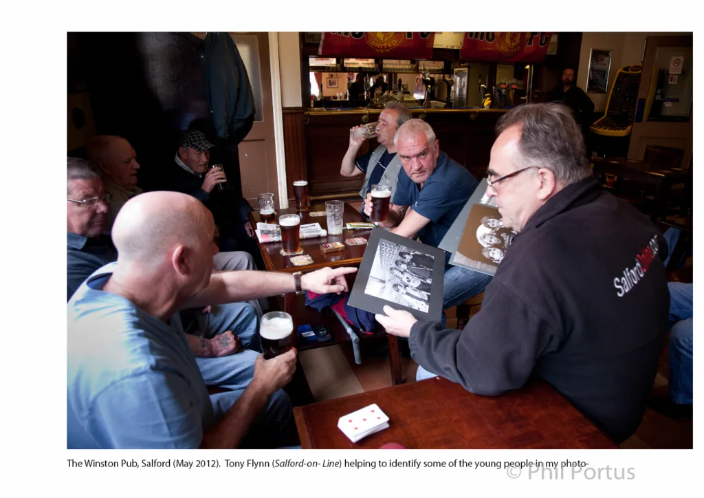 Several men sit at a table in a pub, looking at a photo album.