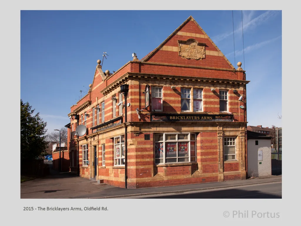 A three-story brick building with multiple windows and a sign reading "BRICKLAYERS ARMS" is visible under a blue sky.