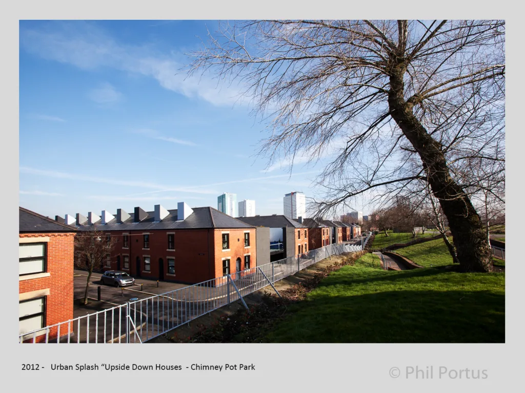 Rows of brick houses with a bare tree branch extending over a grassy area under a blue sky.