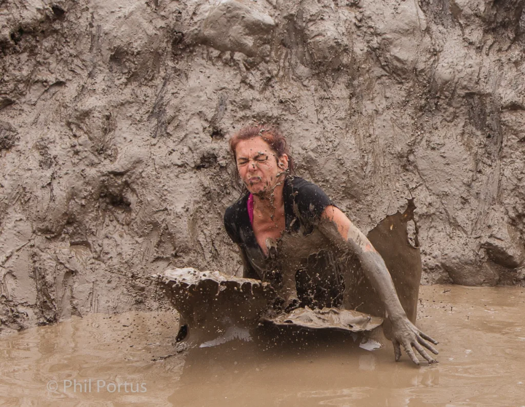 A person covered in mud pushes upward through a thick layer of muddy water.
