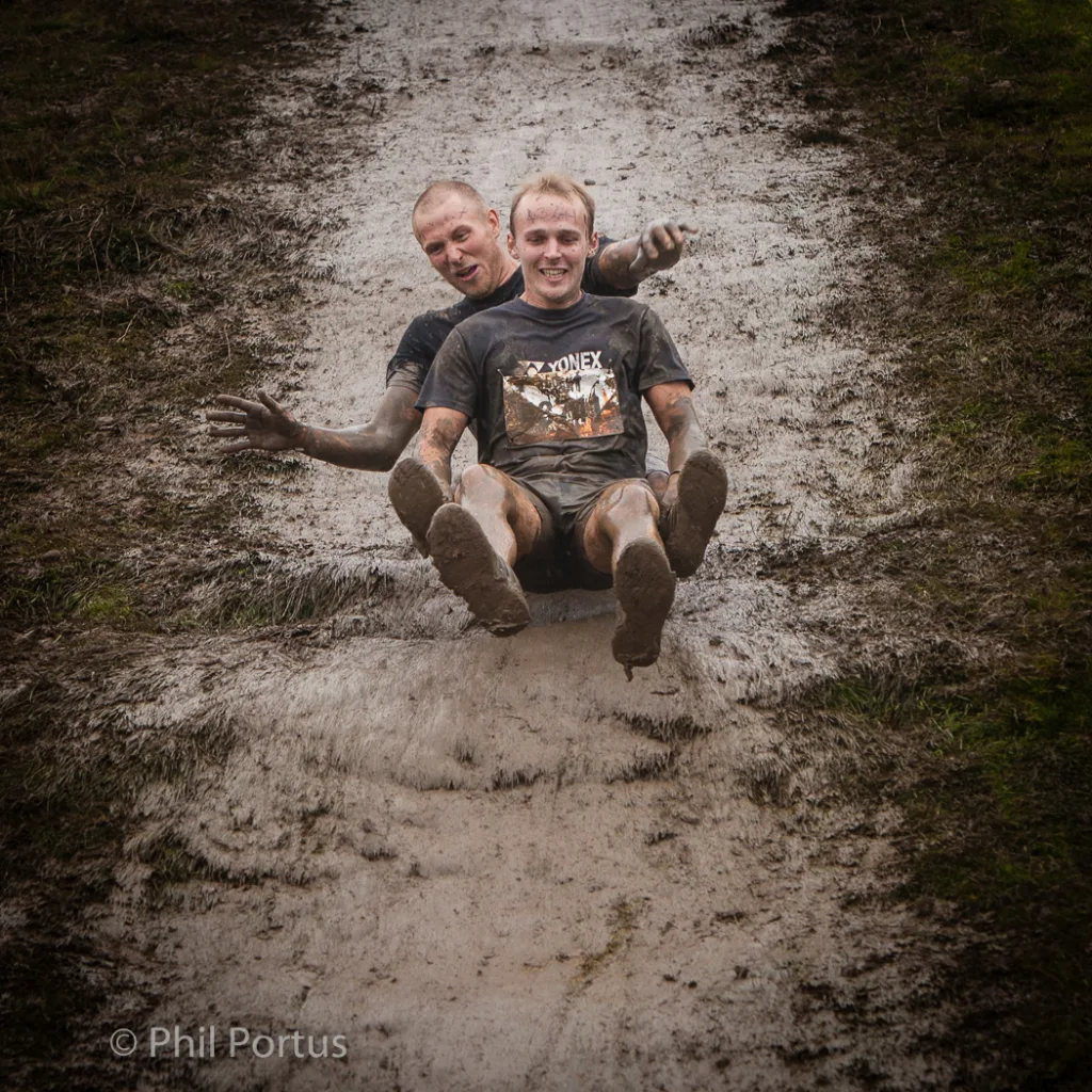 Two people slide down a muddy slope, covered in dirt and smiling.