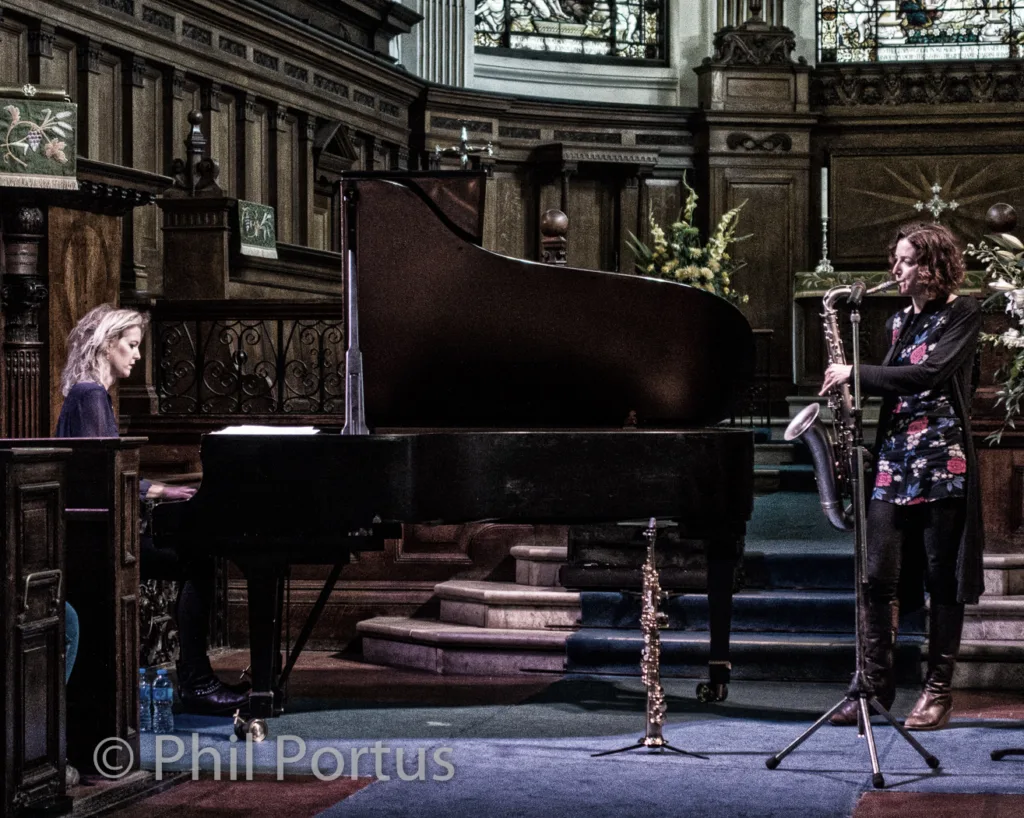 Two musicians perform on a stage with a grand piano and saxophone.