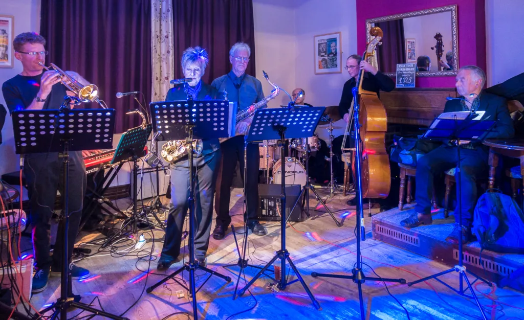 A jazz band performs on a stage with music stands and blue lighting.