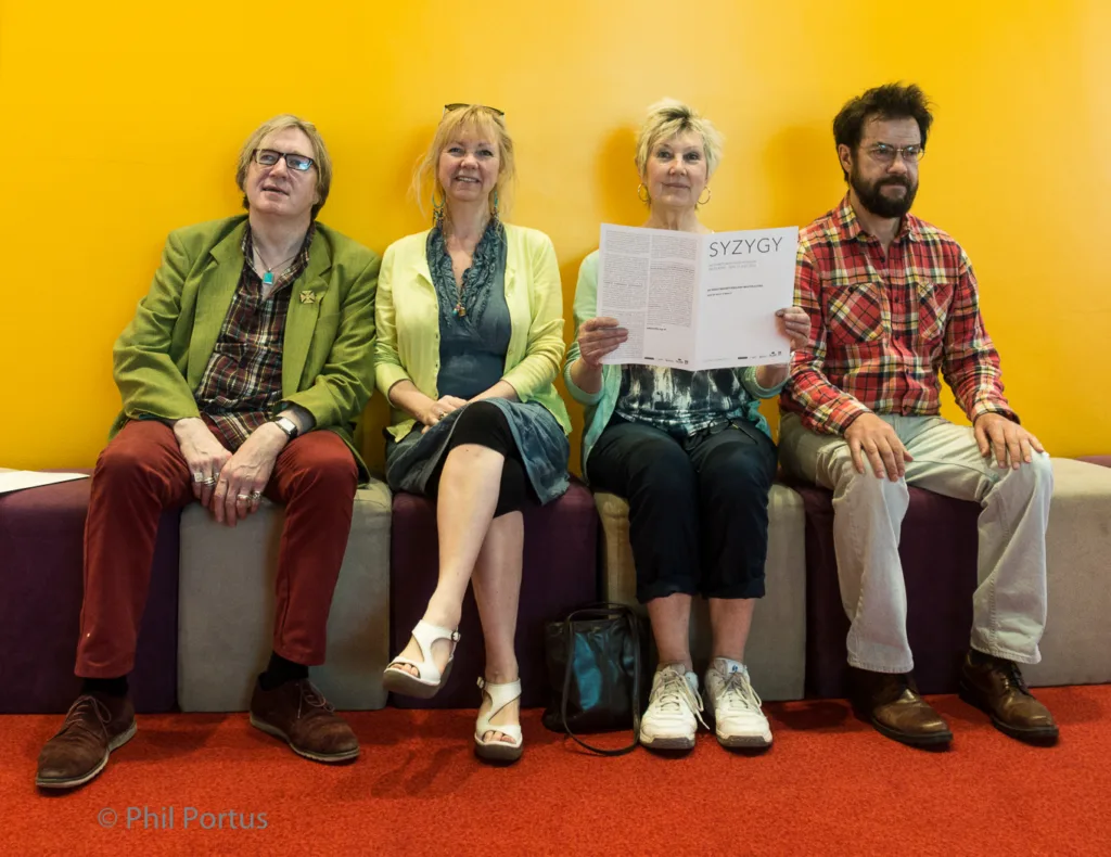 Four people sit on a purple bench against a bright yellow wall.