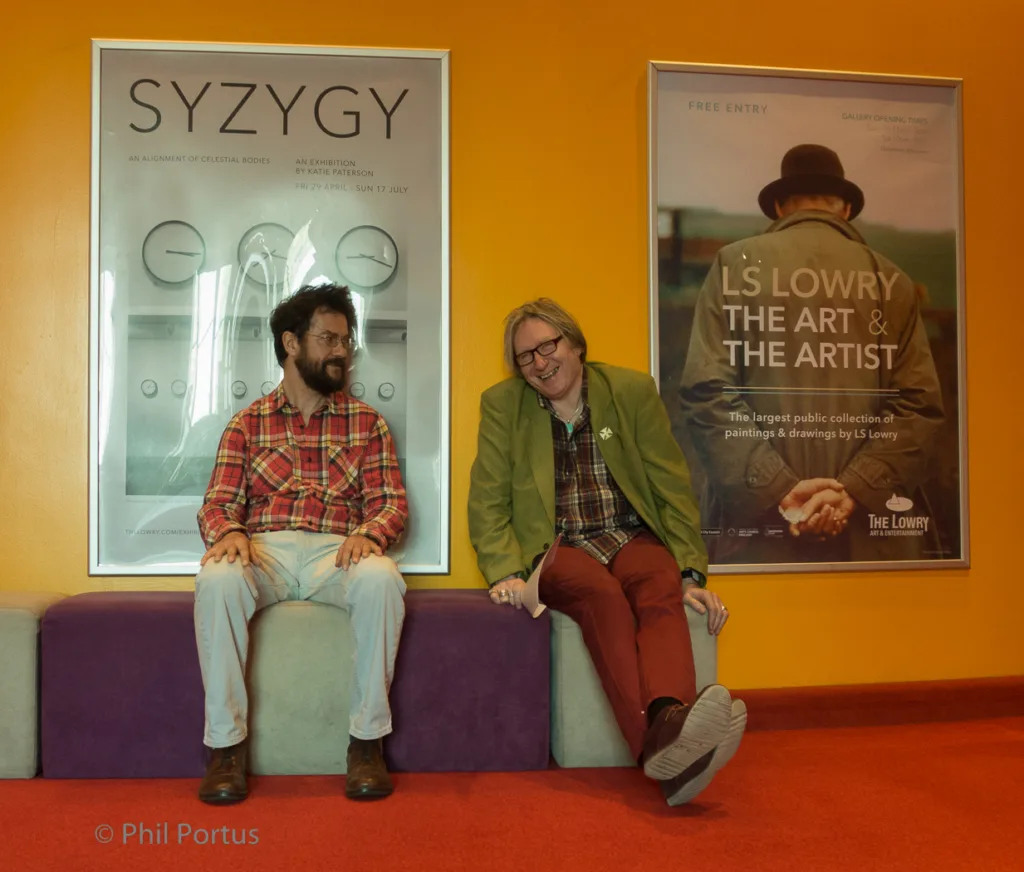 Two people sit on a purple bench in front of posters with text and graphic design.