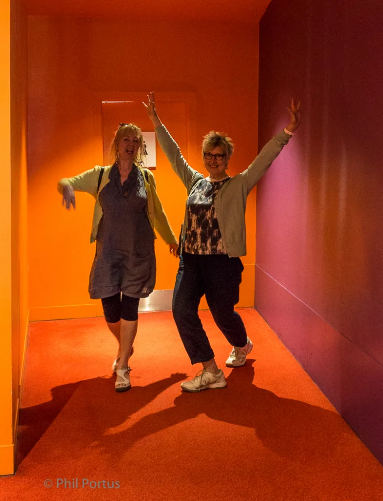 Two people with arms raised are smiling while walking down a brightly colored hallway.