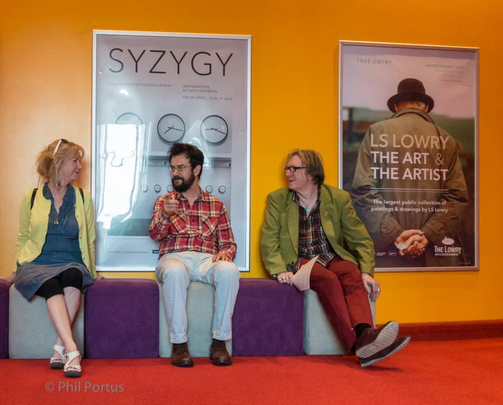 Three people sit on a purple bench in front of posters with text and graphic designs.