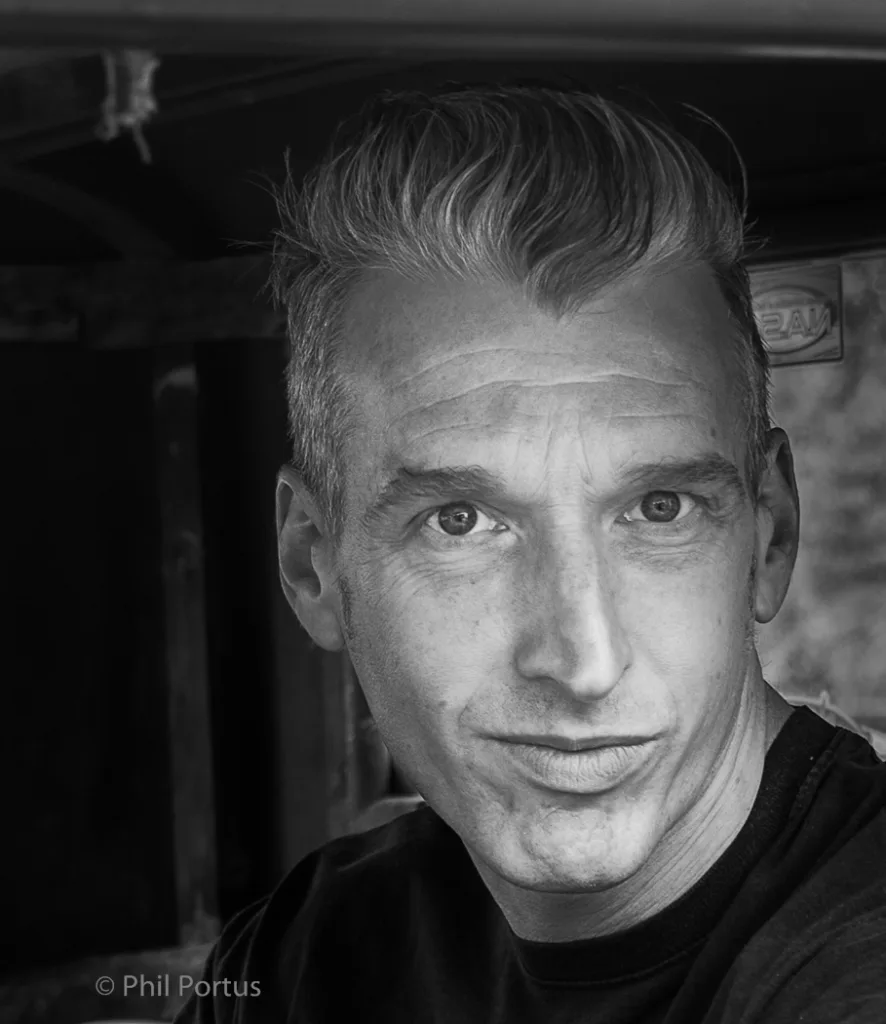 A black and white portrait shows a person with styled hair looking directly at the camera.
