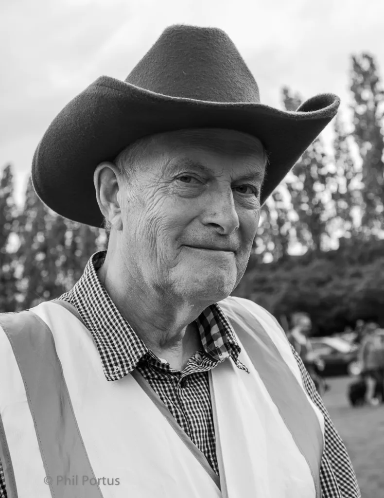 A man wearing a cowboy hat and vest looks directly at the camera in black and white.
