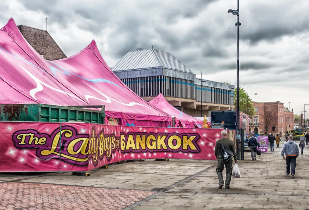 A pink tent with a sign stands in front of a large building under an overcast sky.