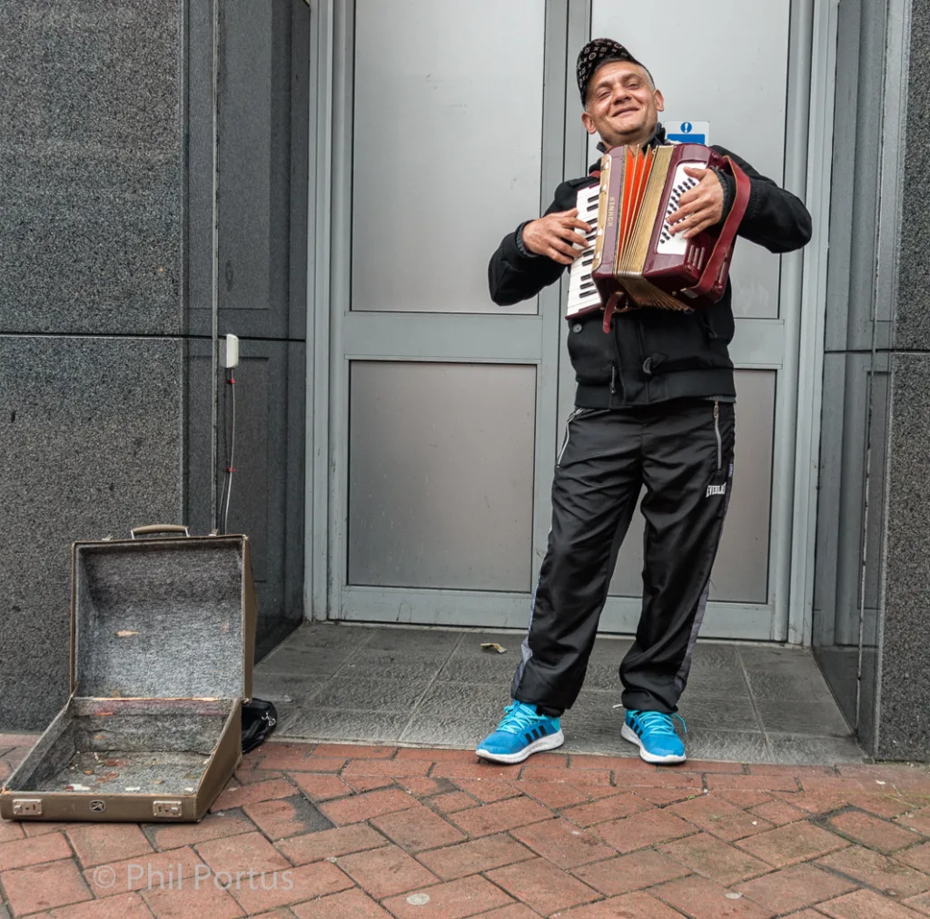 A person stands holding an accordion near a doorway with an open suitcase on the ground.