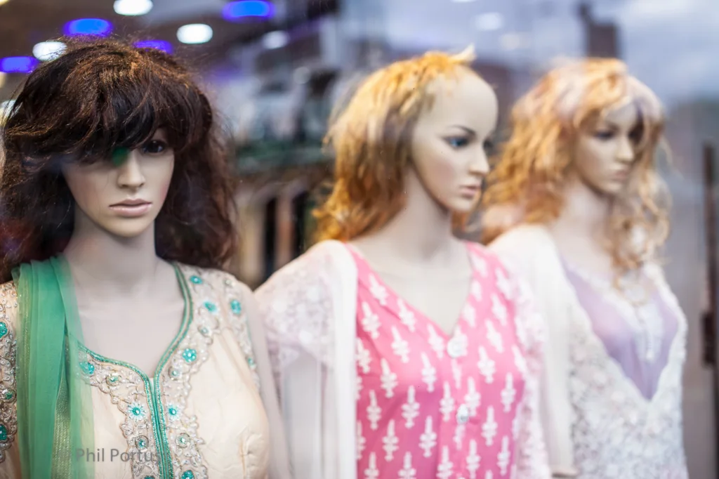 Three mannequins wearing colorful dresses stand in a store window display.