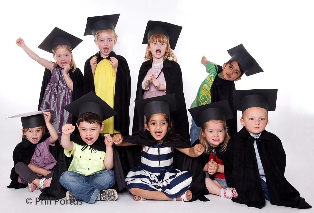 A group of young children wearing graduation caps and gowns pose for a studio portrait.