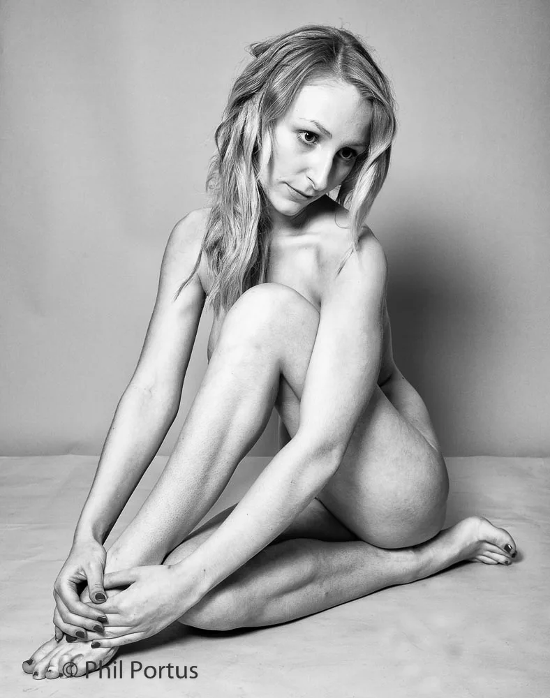 A person sits cross-legged on a plain surface in black and white portrait.