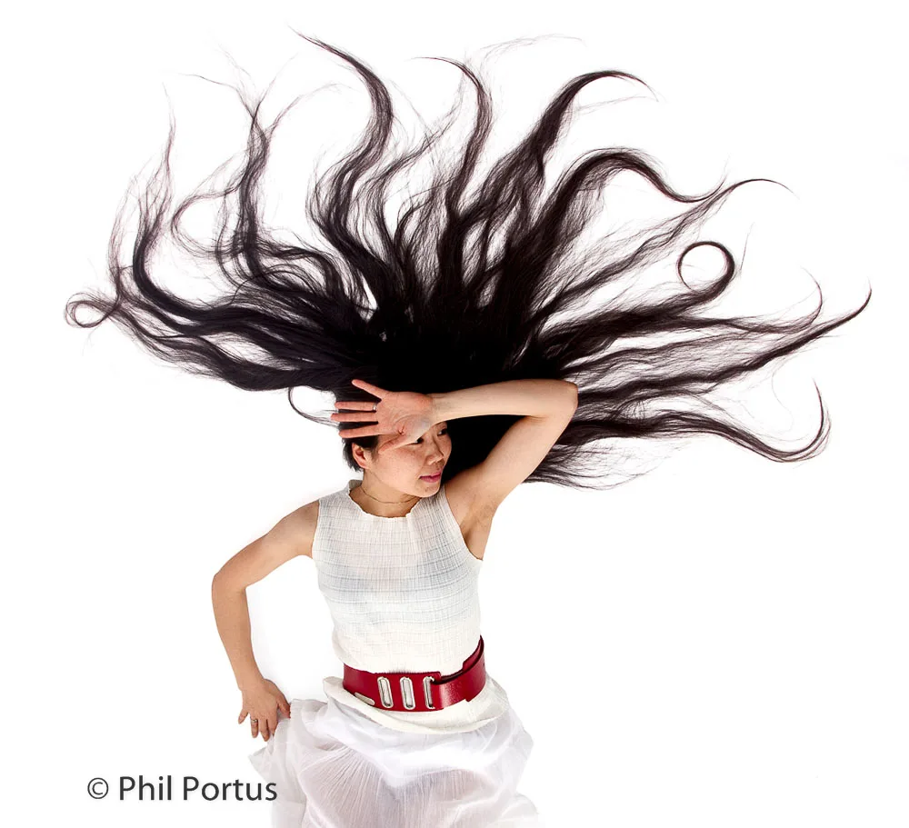 A person with long dark hair styled around their head poses against a white background.