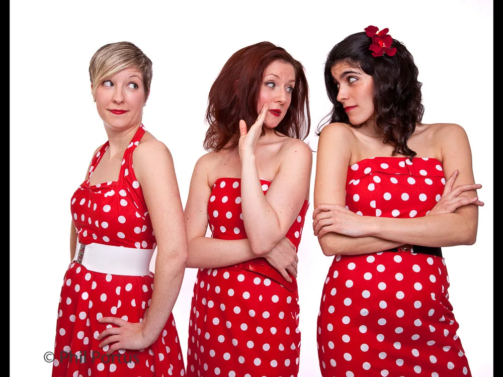 Three women in red polka dot dresses with different expressions pose against a white background.