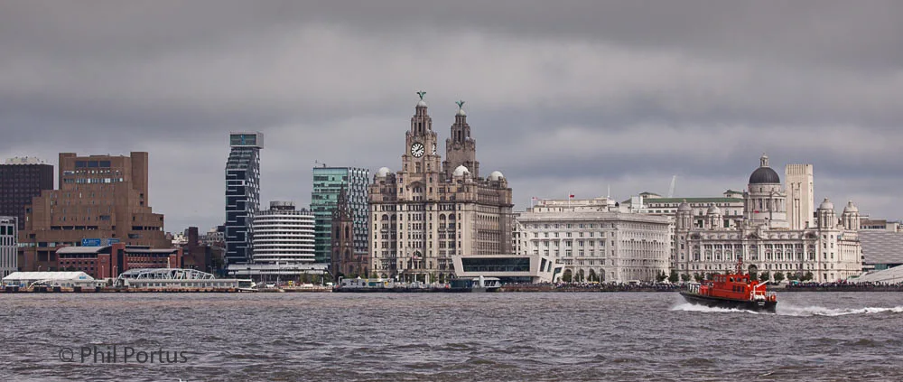 A cityscape rises from a body of water under an overcast sky with a boat moving across the foreground.