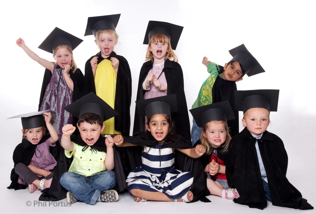 A group of young children wearing graduation caps and gowns pose for a studio portrait.