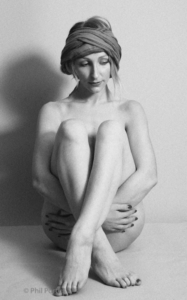 A person with a head covering sits cross-legged on a surface in black and white.