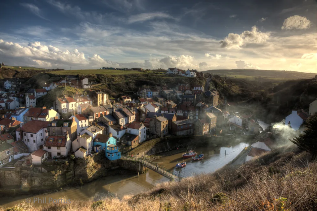A hillside village with colorful buildings sits nestled in a valley below a dramatic sky.