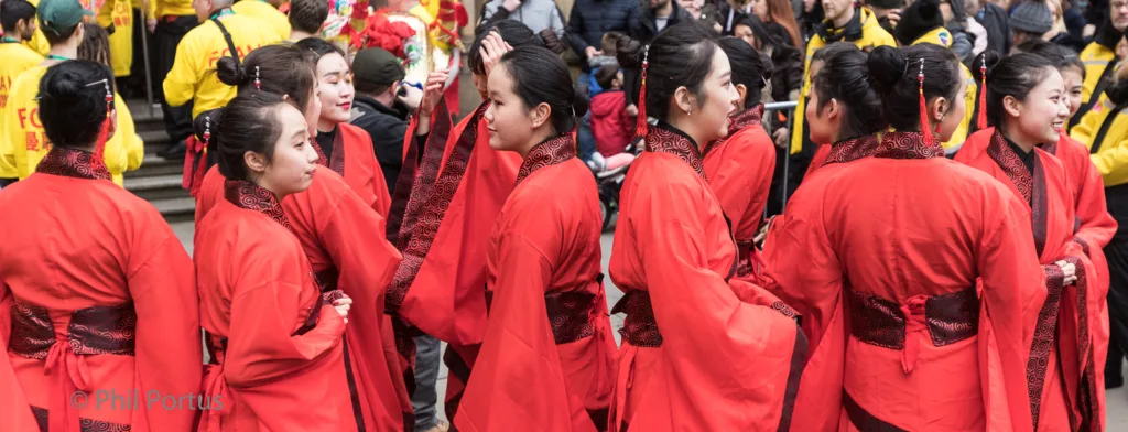 A group of performers wearing red traditional clothing stand in a crowd with people in yellow and red.
