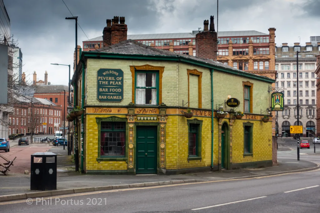 A yellow brick building with dark green trim and signage stands on a street corner under an overcast sky.