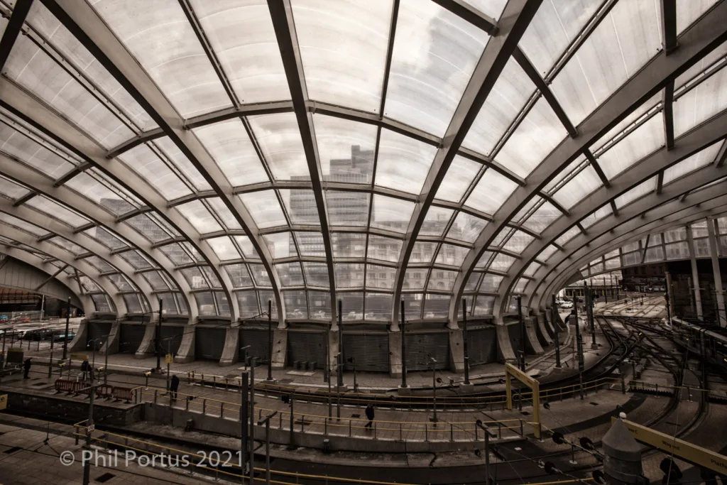 A large arched structure with a glass roof overlooks train tracks and platform edges.