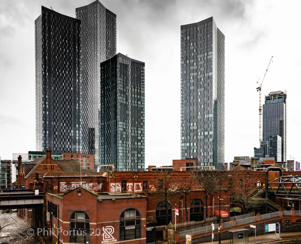 Tall modern buildings rise above older brick structures under a cloudy sky.