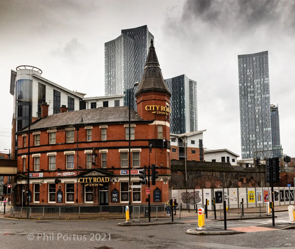 A brick building with a turret sits in front of several tall, modern glass buildings under an overcast sky.