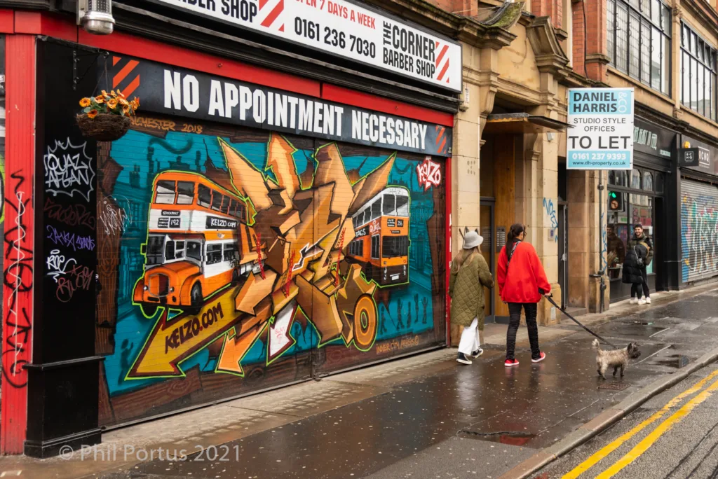 A storefront with a vibrant mural of buses and abstract shapes is visible on a wet street.