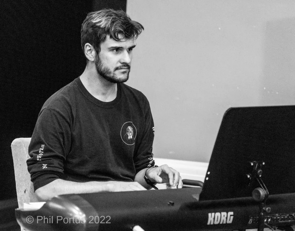 A person with dark hair sits at a keyboard, looking down and playing.