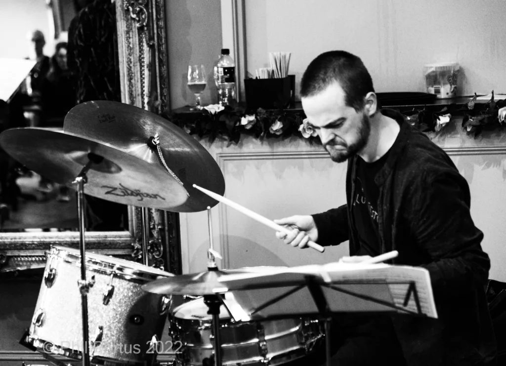 A drummer plays a drum kit during a performance in black and white.