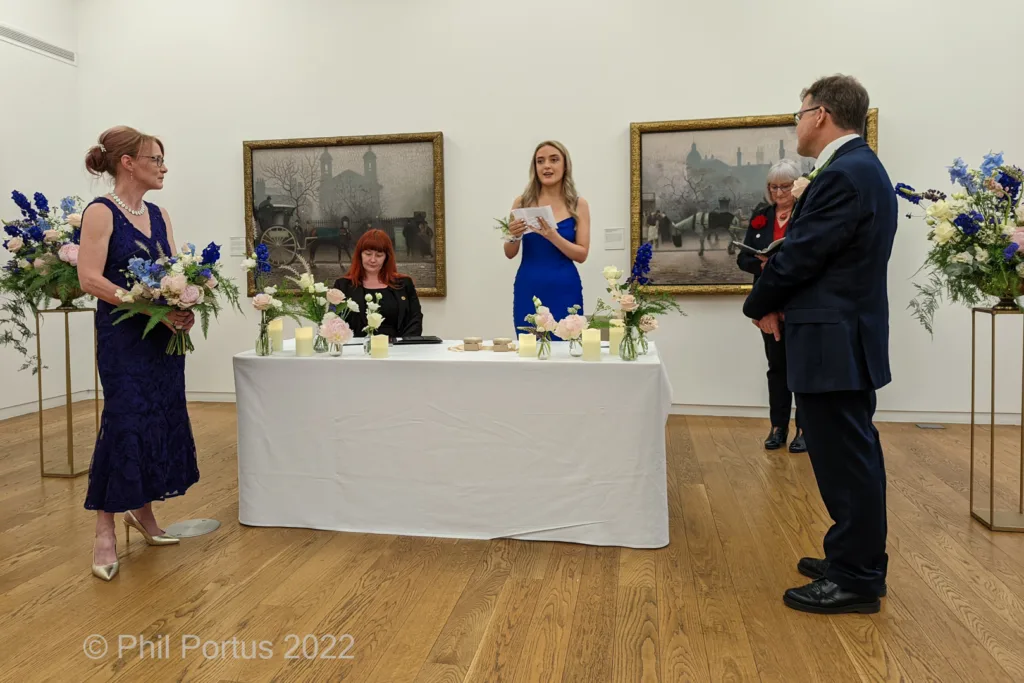 A wedding ceremony takes place indoors with several people gathered around a decorated table.