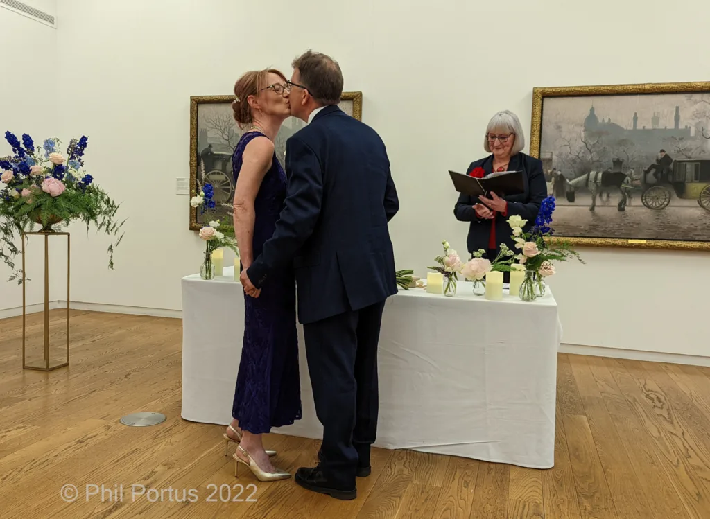 A couple embraces at a small table decorated with flowers during what appears to be a wedding ceremony.