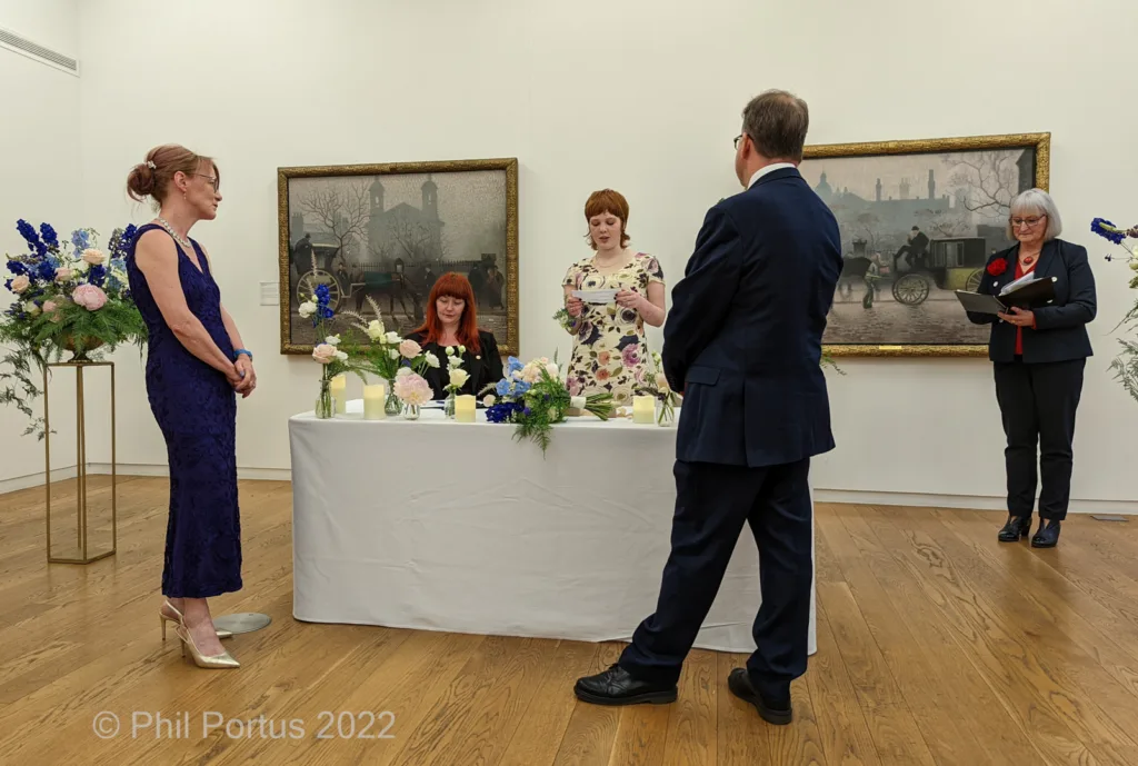 Four people stand around a draped table in a room with two framed paintings on the walls.