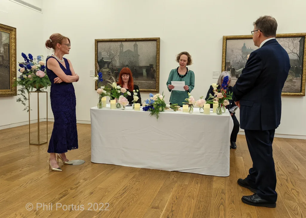 Four people stand around a draped table in a room with framed artwork on the walls.