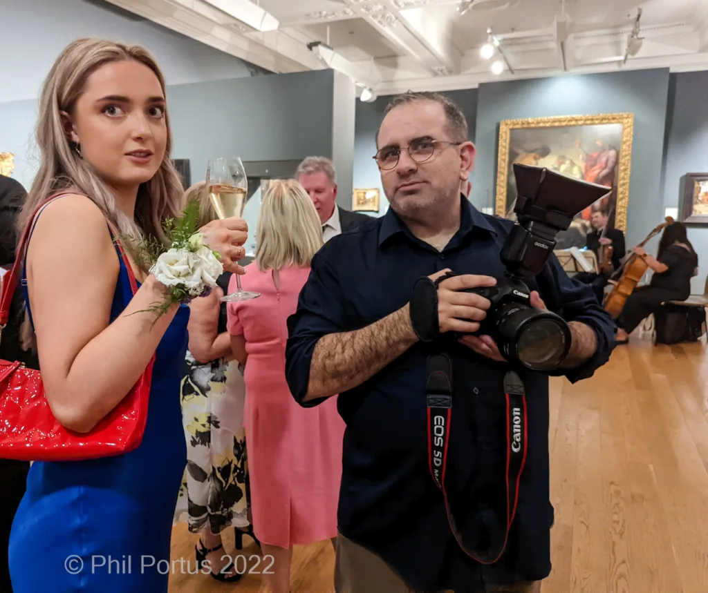 A person with a camera takes a picture of a woman holding champagne at an event.