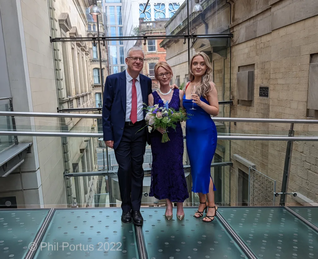Three people pose on a glass walkway with an urban building backdrop.