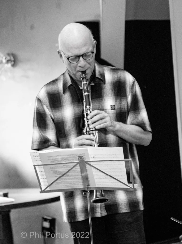 A man with glasses plays a clarinet while looking down at sheet music on a stand.