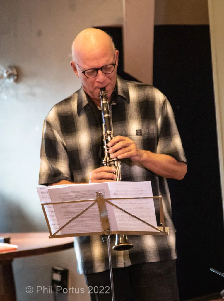 A person with glasses plays a clarinet while looking down at sheet music on a stand.