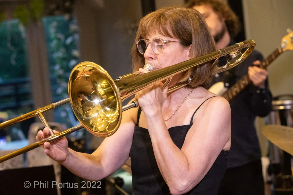 A musician plays a brass instrument while wearing glasses and a black top.