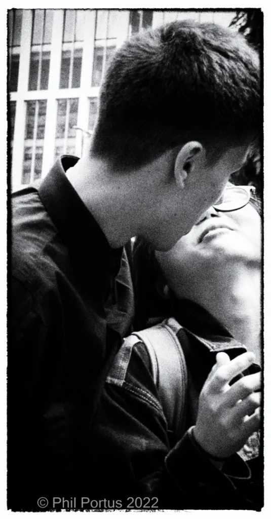 Two people embrace closely in black and white, with a window visible behind them.